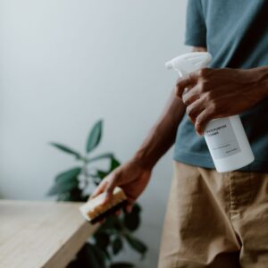 A man using a multi-purpose cleaner and sponge to clean a table indoors, emphasizing hygiene.