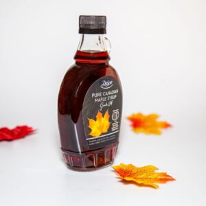 Close-up of a Canadian maple syrup bottle with colorful autumn leaves on white background.