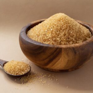 Close-up of raw brown sugar in a rustic wooden bowl with a spoon on a beige background.