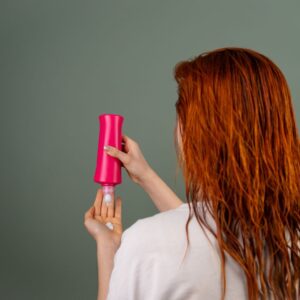 Adult woman with wet red hair applying conditioner. Hair care routine.