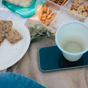A cozy outdoor picnic setup with snacks, a smartphone, and a drink on a blanket.