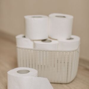 Collection of toilet paper rolls neatly arranged in a woven basket on a wooden floor, indicating hygiene and cleanliness.