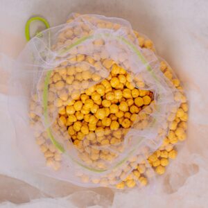 A top view of yellow chickpeas in an eco-friendly mesh bag on a neutral background.