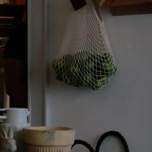 White mesh bag filled with green produce hanging on wall.
