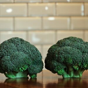 Two heads of fresh broccoli on a wooden table.