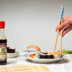 a person holding chopsticks over a plate of sushi