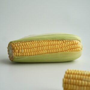 Partially husked ear of corn on a white surface.